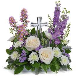 White roses and purple flowers arranged around a clear glass cross