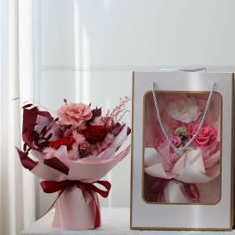 Bouquet of pink and red roses in pink wrapping beside a gift bag