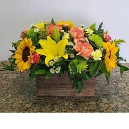 Mixed bouquet in a wooden box with sunflowers, lilies, and pink carnations