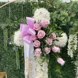 Pink roses and white chrysanthemums arranged on a standing cross with a ribbon