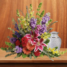 Mixed bouquet with lilies, roses, and purple blooms beside a decorative urn