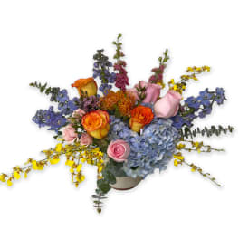 Mixed bouquet with blue hydrangeas, orange roses, and pink blooms in a vase