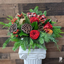 Red roses with pine, berries, and plaid ribbon in a white pedestal vase