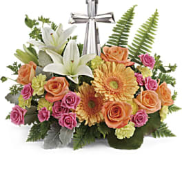 Mixed bouquet with white lilies, roses, and gerbera daisies topped by a silver cross