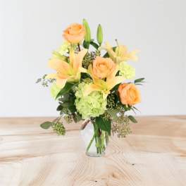 Peach roses and pale lilies in a clear glass vase