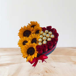 Heart-shaped bouquet of sunflowers, red roses, and chocolates with a red ribbon