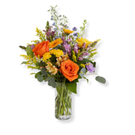 Tall mixed bouquet with orange roses, yellow and purple flowers in a clear glass vase