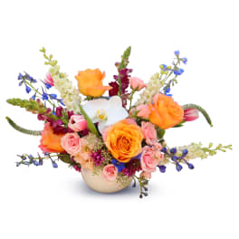 Colorful bouquet of roses, orchids, and blue flowers in a round vase