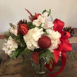 Holiday bouquet of white flowers with red ornaments and ribbon in a glass vase