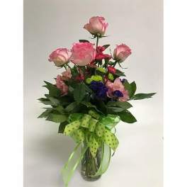 Pink roses and mixed flowers in a clear glass vase with a green ribbon