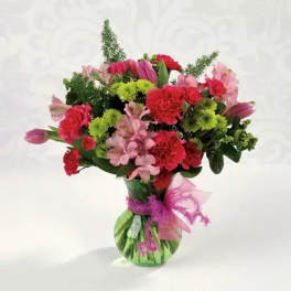 Mixed bouquet of pink and red flowers in a green glass vase