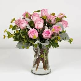 Pink roses arranged in a clear glass vase with greenery