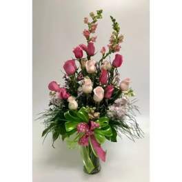 Tall bouquet of pink and white roses in a glass vase with a ribbon bow