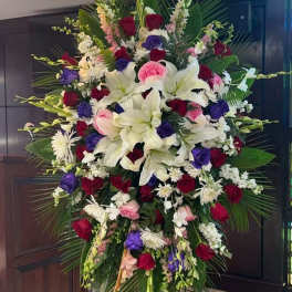 Large standing floral spray with white lilies, red and purple roses, and pink accents