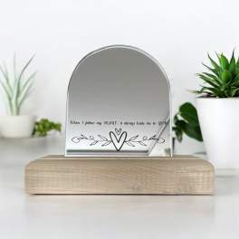 A small arched mirror on a wooden base with a heart design and text.