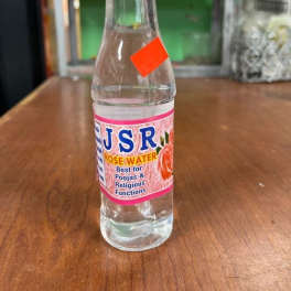 Bottle of rose water with a pink label on a wooden table
