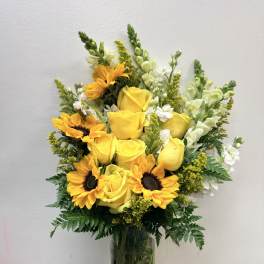 Yellow roses and sunflowers in a clear glass vase