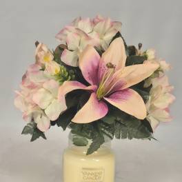 Pink and cream flowers arranged in a glass candle jar
