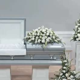 White floral casket spray on a silver casket in a funeral room