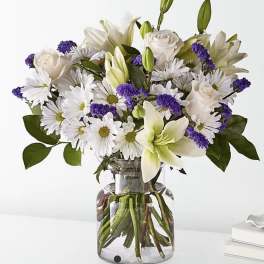 White lilies, roses, and daisies in a clear glass vase