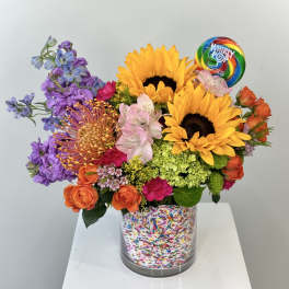 Colorful bouquet with sunflowers, roses, and a lollipop in a sprinkle-covered vase