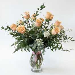 Peach roses in a clear glass vase with mixed greenery