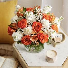Orange and white rose bouquet in a glass vase on a table