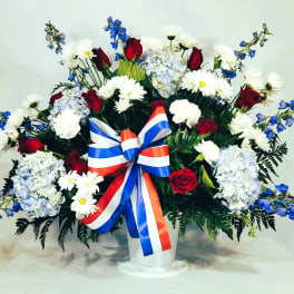 Large red, white, and blue floral arrangement in a white vase with a ribbon bow