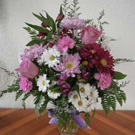 Mixed pink and white bouquet in a glass vase with a purple ribbon