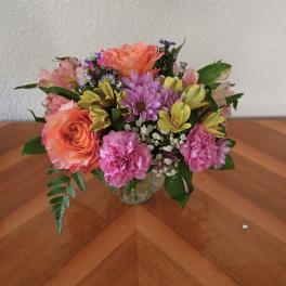 Mixed bouquet of roses, carnations, and daisies in a clear glass vase