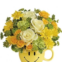 Yellow and white flower arrangement in a smiley-face mug