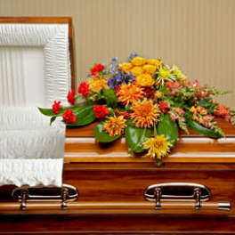 Bright mixed casket spray with orange and yellow flowers arranged on a wooden casket