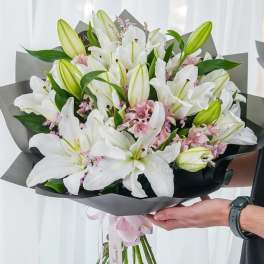 Bouquet of white lilies and pink filler flowers wrapped in dark paper