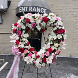 Heart-shaped floral wreath with pink, red, and white flowers on a stand