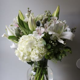 White floral bouquet in a clear glass vase with lilies and hydrangea