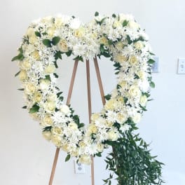 Heart-shaped white floral wreath on a wooden easel with trailing greenery