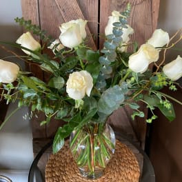 Tall arrangement of white roses and eucalyptus in a clear glass vase