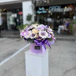 Lavender and white bouquet in a pink hatbox with a purple ribbon