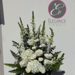 White floral arrangement in a vase with tall greenery and roses