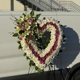 Heart-shaped floral wreath with pink roses and white flowers on an easel