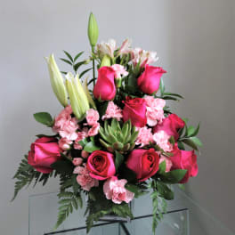 Pink roses and lilies arranged in a clear vase with greenery.