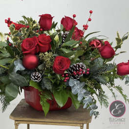 Red roses arranged in a red container with pinecones and berries