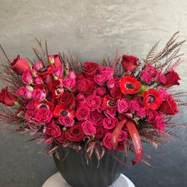 Red and hot pink roses arranged in a black vase with red ribbon