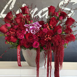Red rose arrangement in a silver vase with trailing burgundy accents