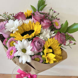 Bouquet of pink roses, sunflowers, and white daisies wrapped in brown paper