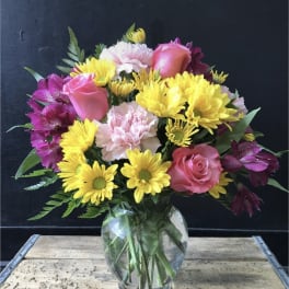 Mixed bouquet of pink roses, yellow daisies, and purple alstroemeria in a glass vase