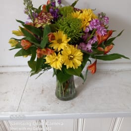 Mixed bouquet of yellow, purple, and orange flowers in a glass vase