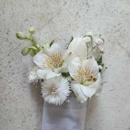 White floral corsage with lilies and small white blooms on a ribbon wrap