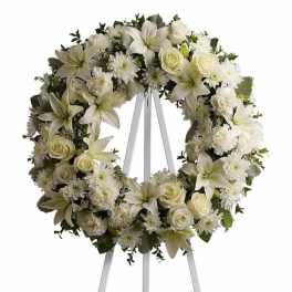 White floral wreath of lilies, roses, and mums displayed on a white easel stand