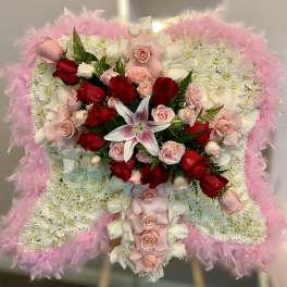 Standing angel-wing floral arrangement of white mums with pink feathers, roses, and a lily.
